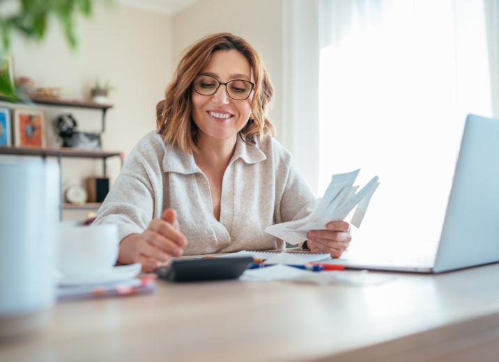 A woman using a calculator and laptop to manage accounts payable for her small business.