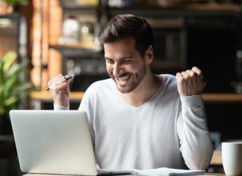 Excited employee reading company newsletter on laptop