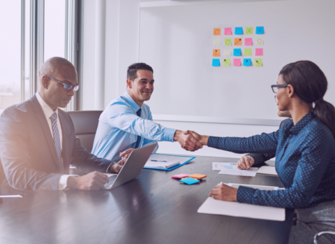 Two business colleagues shaking hands across the table in congratulations during a multiracial business meeting at a conference table in the office
