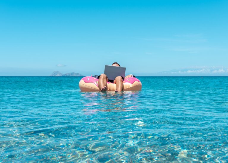 Businessman using laptop computer on an inflatable donut in the sea.