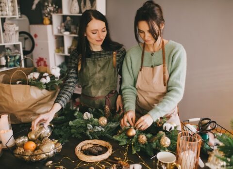 Two women decorating their business using a garland and ornaments.