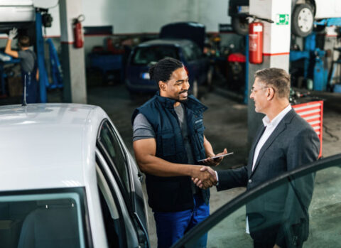 A car mechanic shaking hands with a customer in a garage.