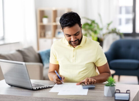 A small business owner sitting at a desk in his living room and preparing a balance sheet.