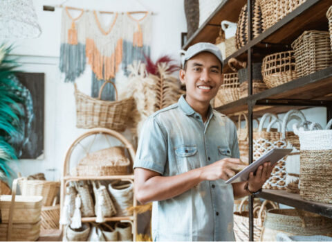 A wicker shop owner holds a tablet and reviews his inventory to avoid cash flow issues.
