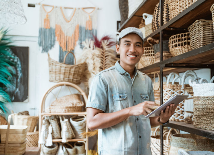 A wicker shop owner holds a tablet and reviews his inventory to avoid cash flow issues.
