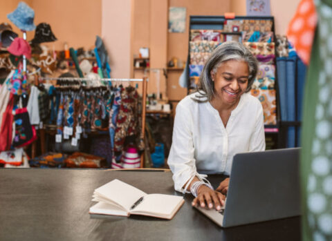 A fabric merchant working on a cash flow projection using a laptop in her shop.