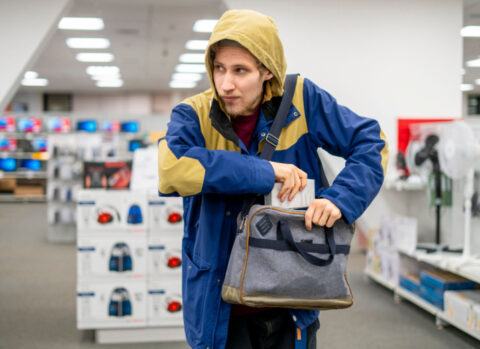 A shoplifter looks over his shoulder as he pockets a small gadget in an electronics store.
