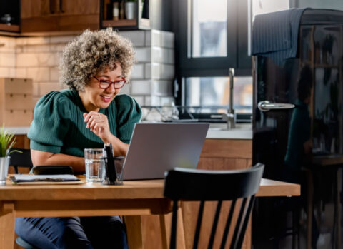 A small business owner sitting at her kitchen table uses a laptop to prepare an income statement.