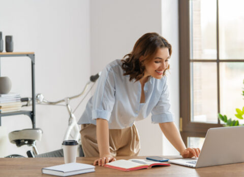 A small business owner leaning towards her laptop to send an ACH transfer to a vendor.
