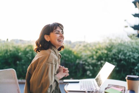 Smiling professional working remotely outdoors with a laptop, symbolizing the freedom of nomadic accounting.