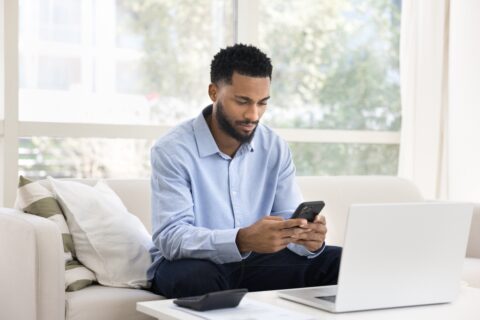 Focused professional using phone and laptop in a bright home office