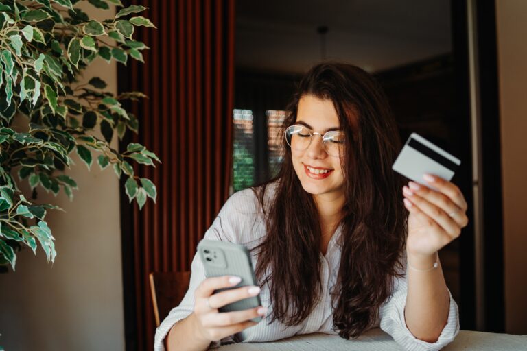 Happy woman making online payment with smartphone and credit card at home.