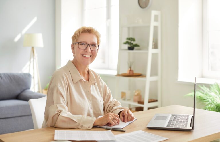 Smiling accountant working at a desk with a laptop and financial documents, representing modern accounting practices and technology adoption.
