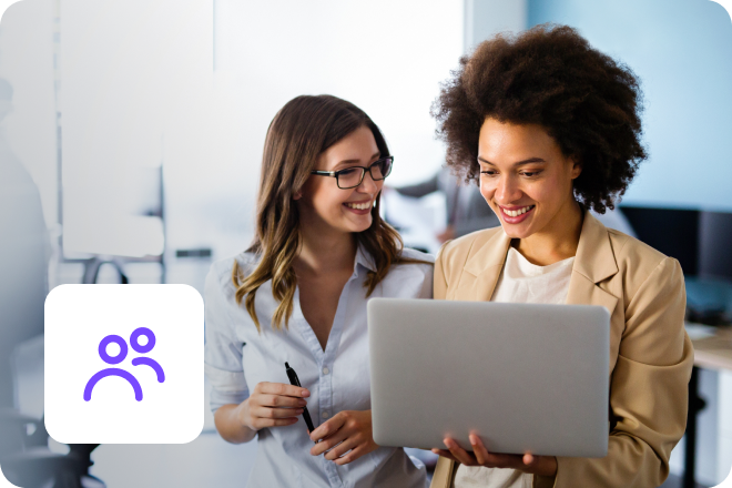 A pair of smiling female colleagues working in an office on a laptop.