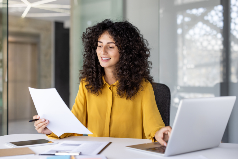 Business professional reviewing W-9 form and vendor documentation while managing contractor payments on laptop in office